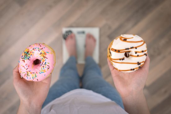 A woman stands on the scales, holds donuts in her hands, top view, copy space. A woman stands on the scales, holds donuts in her hands, the concept of diet, weight gain, weight loss, proper nutrition, sweet.