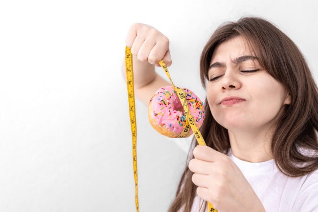 Young woman holding donut with measuring tape, concept of diet, calorie food, overeating, weight gain set.